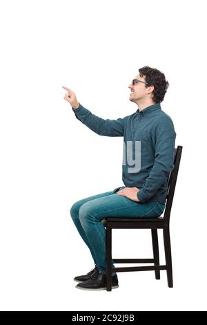 Side view full length portrait of cheerful businessman seated on a chair hand outstretched as pressing an invisible object or screen with his index fi Stock Photo