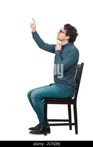 Side view full length portrait of thoughtful businessman sitting on chair hand under chin, pressing an invisible object or screen with his index finge Stock Photo