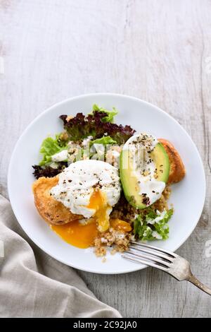 A healthy and balanced breakfast plate. Benedict's egg spreads on a toasted toast with half an avocado, quinoa and lettuce, seasoned   spices and yogu Stock Photo