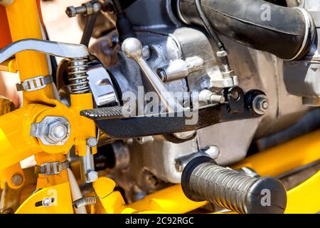 Pedal of a brake of the motorcycle of black color, against the background of the yellow and chromeplated details. Stock Photo
