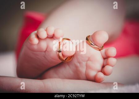 Close up of baby's feet with wedding rings in mother's hands. Ne Stock Photo