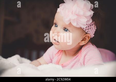 Close-up portrait of cute 3 months old surprising baby girl in pink lying down on a white bed at home. Big open eyes. Healthy little kid shortly after Stock Photo