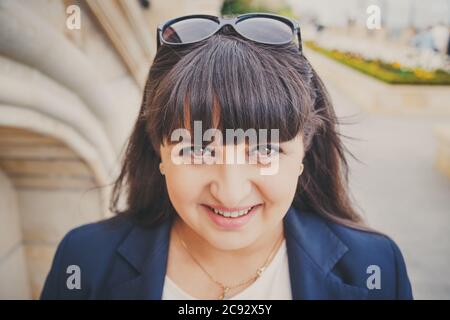 Portrait of happy smiling beautiful overweight young woman in dark blue jacket outdoors at the street. Confident fat young woman. Xxl woman, plus size Stock Photo