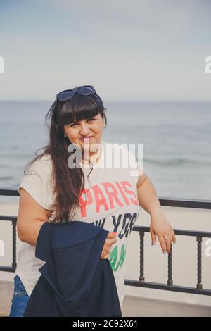 Portrait of happy smiling beautiful overweight young woman in white T-shirt and dark blue jacket outdoors at the street. Confident fat young woman Stock Photo