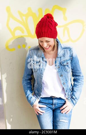 Smiling woman with jeans clothes leaning against painted wall Stock Photo