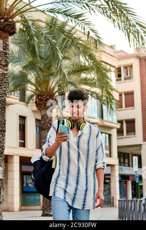 Young afro-haired man is walking down the street looking at his mobile Stock Photo