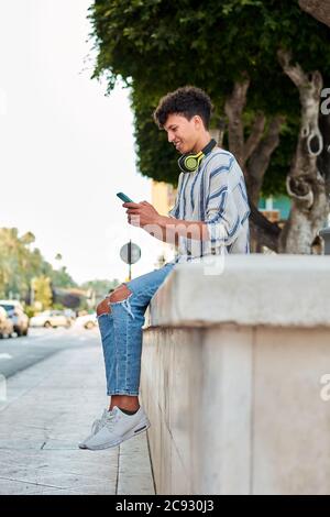 Young man with afro hair smiles while he is using his smartphone Stock Photo