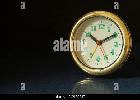 The Old round watch on black background. The Alarm clock on table with reflection. Green numbers and black arrows beside mechanical hours Stock Photo