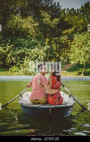 Young beautiful happy loving couple rowing a small boat on a lake. A fun date in nature. Couple hugging in a boat. Stock Photo