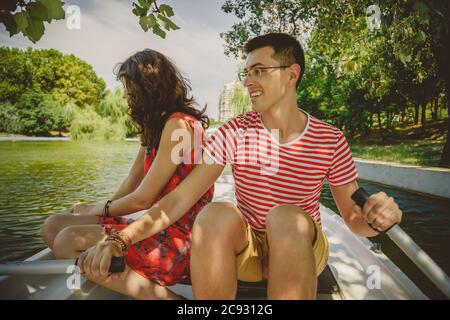 Young beautiful happy loving couple rowing a small boat on a lake. A fun date in nature. Couple in a boat. Stock Photo