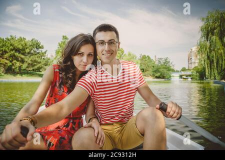 Young beautiful happy loving couple rowing a small boat on a lake. A fun date in nature. Couple in a boat. Stock Photo