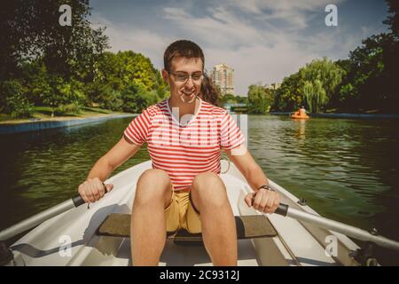 Young beautiful happy loving couple rowing a small boat on a lake. A fun date in nature. Couple in a boat. Stock Photo