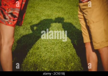 A kiss of shadows. Young romantic couple kissing in the flower park on the grass outside Stock Photo