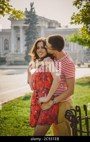Beautiful young smiling couple in love, hugging, kissing and spending time together outdoors at green city street Stock Photo
