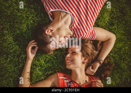 Young loving couple lying together head to head on a grass at summer. Both in red clothes and holding hands. Overhead top view Stock Photo