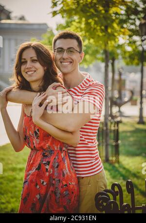 Beautiful young smiling couple in love, hugging and spending time together outdoors at green city street Stock Photo