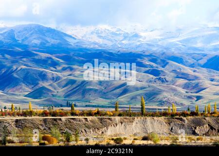 Countryside of Kyrgyzstan in Issyk Kul Region. Grass land with snow caped mountains of Tian Shan mountain range partially seen behind clouds. Stock Photo