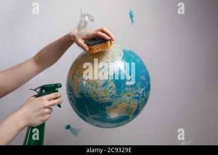 Woman's hand holding a sponge and spray to clear the planet Earth. The concept of improving the state of the environment, Earth Day. Stock Photo