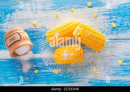 delicious boiled corn and a jar of spilled salt on a wooden white-blue table with top view. Stock Photo