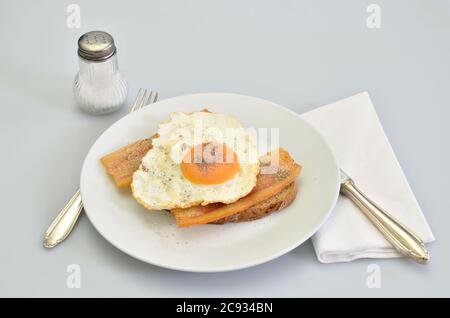 sandwich with bacon and fried egg with salt and pepper on white plate, closeup, isolated on white background Stock Photo