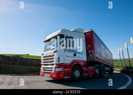 Scania truck pulling a curtainsider trailer negotiating a tight left hand bend on the A623 in the Peak District on a cloudless day Stock Photo