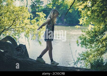 little lovely girl walking on tree trunk in beautiful green nature by the river Stock Photo