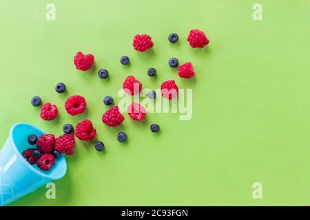 Explosion of different berries. Flat lay with blueberry and raspberry in plastic waffle cone on bright background. Top view. Fresh summer berries in a Stock Photo