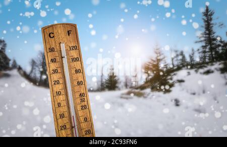Wooden thermometer against a snowy winter landscape background. Cold temperatures with extreme winter weather concept. Stock Photo