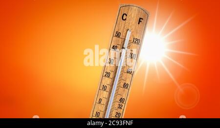 Thermometer against orange background with hot summer sun. Heat wave concept. Stock Photo