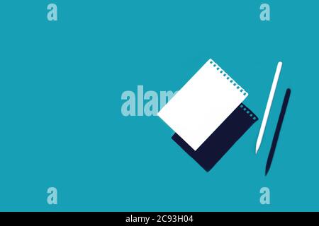 A clean white sheet torn from a spiral pad and a pencil. On a blue background with shadows. Stock Photo