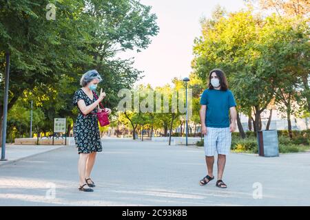 Two friends walking with each other while social standing and wearing masks Stock Photo