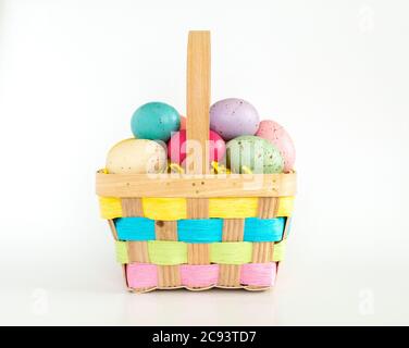 a wicker Easter basket filled with colorful speckled Easter eggs isolated on white Stock Photo