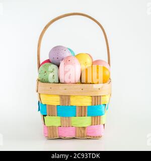 a wicker Easter basket filled with colorful speckled Easter eggs isolated on white Stock Photo