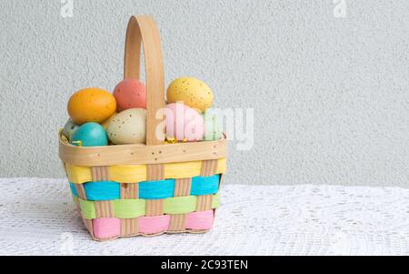 a small wicker Easter basket filled with pastel speckled Easter eggs on a lace tablecloth with copy space Stock Photo