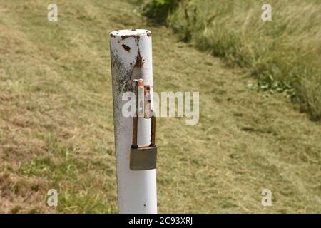 Old rusty padlock locked on white painted pillar of the entrance gate to the field road. Stock Photo