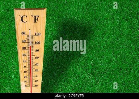 Wooden weather thermometer measurement on a green grass during a hot day. Stock Photo