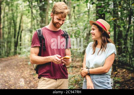Young caucasian couple uses a smartphone to navigate in the forest. Hiking tourists orientation on the terrain using an online map, an application in Stock Photo