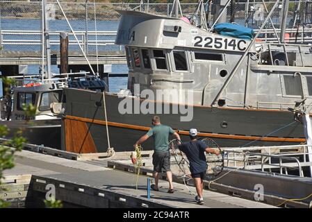 Fisherman carry crab traps past fishing boats moored along docks at Fisherman’s Wharf in Victoria, British Columbia, Canada on Vancouver Island. Stock Photo