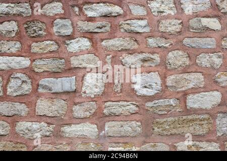 Gray stone wall texture with lime bricks pasted with red colored cement. Stock Photo