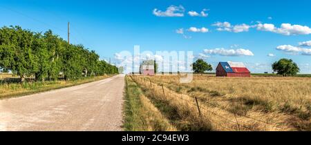An abandoned old barn in Rural Texas with the state flag painted on its roof sits in a farmland community framed by fields and a dirt road. Stock Photo