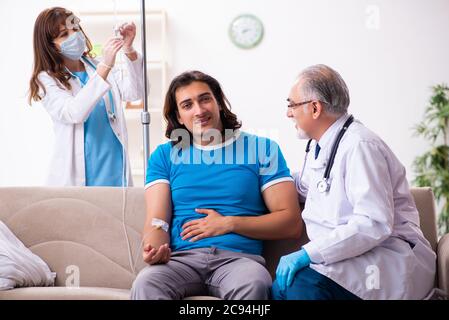 Two doctors visiting sick man at home Stock Photo