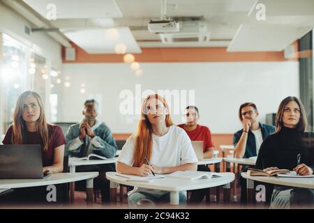 Group of male and female students sitting at their desk and paying attention to the lecture. High school classroom with students studying. Stock Photo