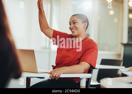 Student asking question whilst attending lecture on campus. Female student raises hand to asks lecturer a question in classroom. Stock Photo