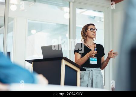 Businesswoman giving presentation in a meeting. Female speaker standing at podium and giving presentation in a conference. Stock Photo
