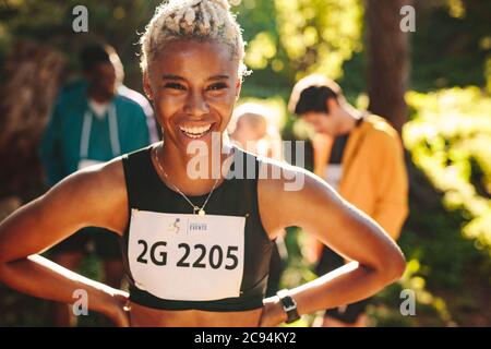 Female cross country marathon runner smiling outdoors. Sportswoman laughing outdoors with her club members in background. Stock Photo