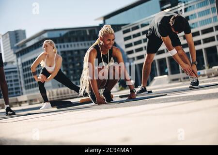 Group of people during workout session outdoors. Friends stretching on exercise mat outdoors in the city. Stock Photo