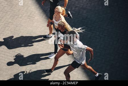 Multi-ethnic group of people running together. Top view of running club members exercising together in the city. Stock Photo