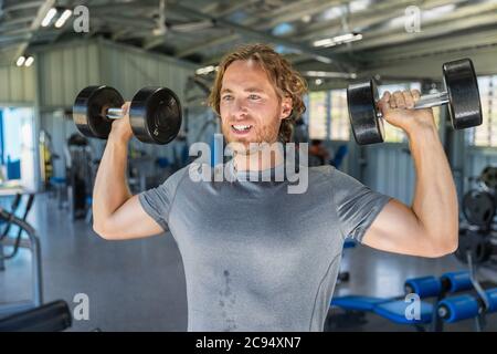 Fitness man doing military presses or standing dumbbell press exercise training in gym with free weights Stock Photo