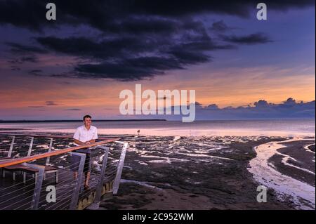 A male tourists enjoys a gorgeous scenic sunrise on the esplanade boardwalk, observation deck in Cairns, Queensland, Australia. Stock Photo