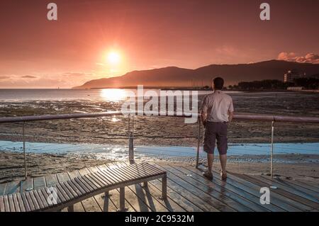 A male tourists enjoys a gorgeous scenic sunrise on the esplanade boardwalk, observation deck in Cairns, Queensland, Australia. Stock Photo